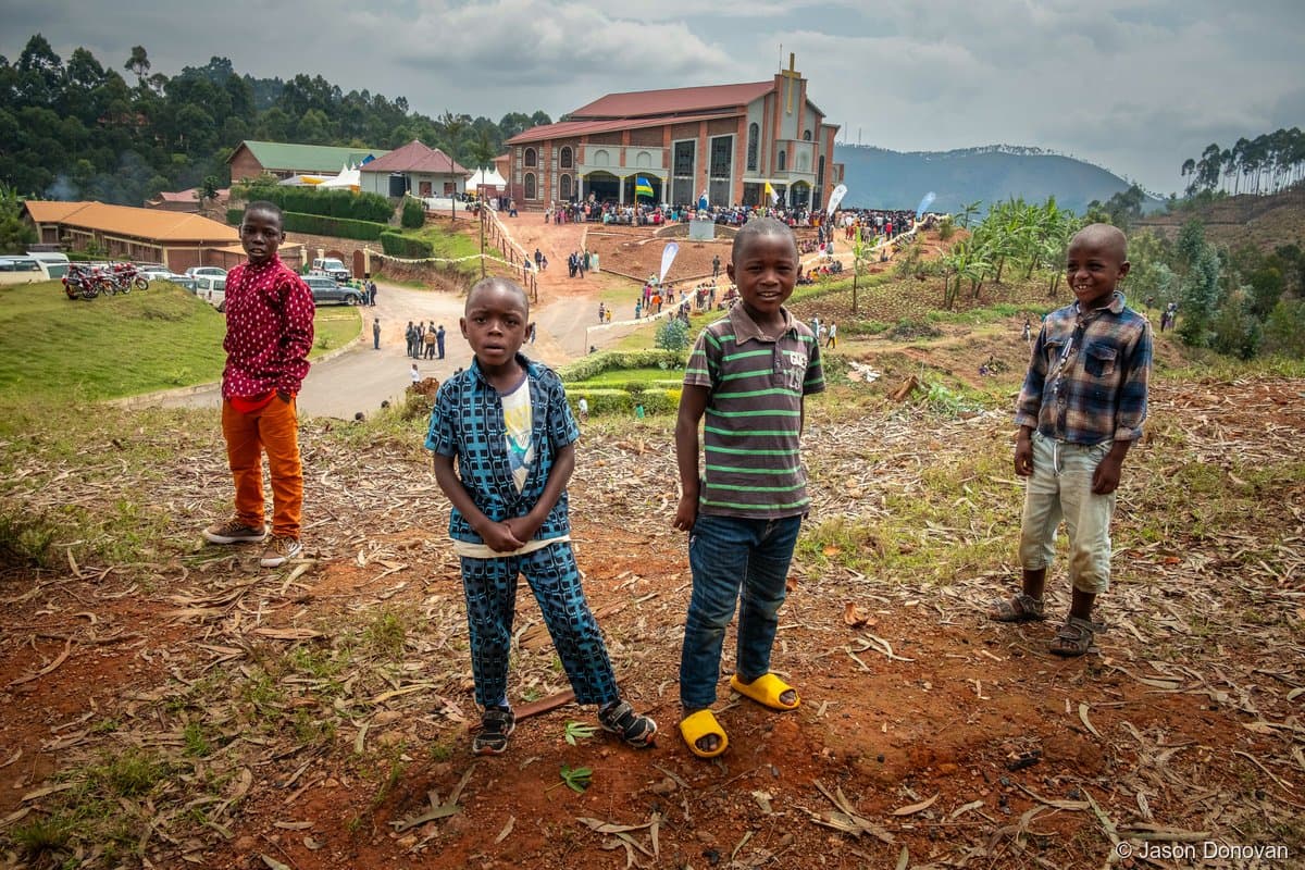 Four boys standing in front of church building on red earth Rwanda