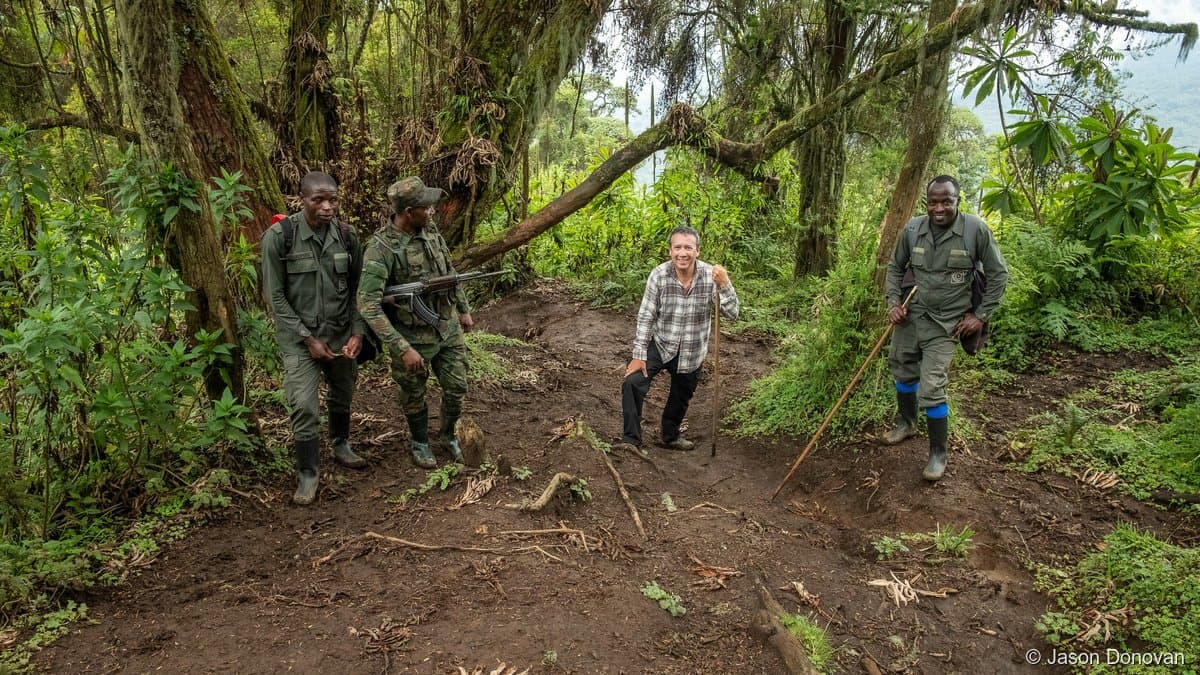 Group of four trekkers with rangers on muddy mountain trail Volcanoes National Park Rwanda